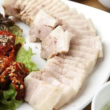 A plate of sliced Bossam, which is boiled pork, served with cabbage wraps and garnishes.