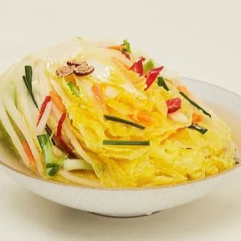 A bowl of Baekimchi, which is a traditional Korean side dish, presented with a mix of vegetables such as radish, cucumber, and scallions.