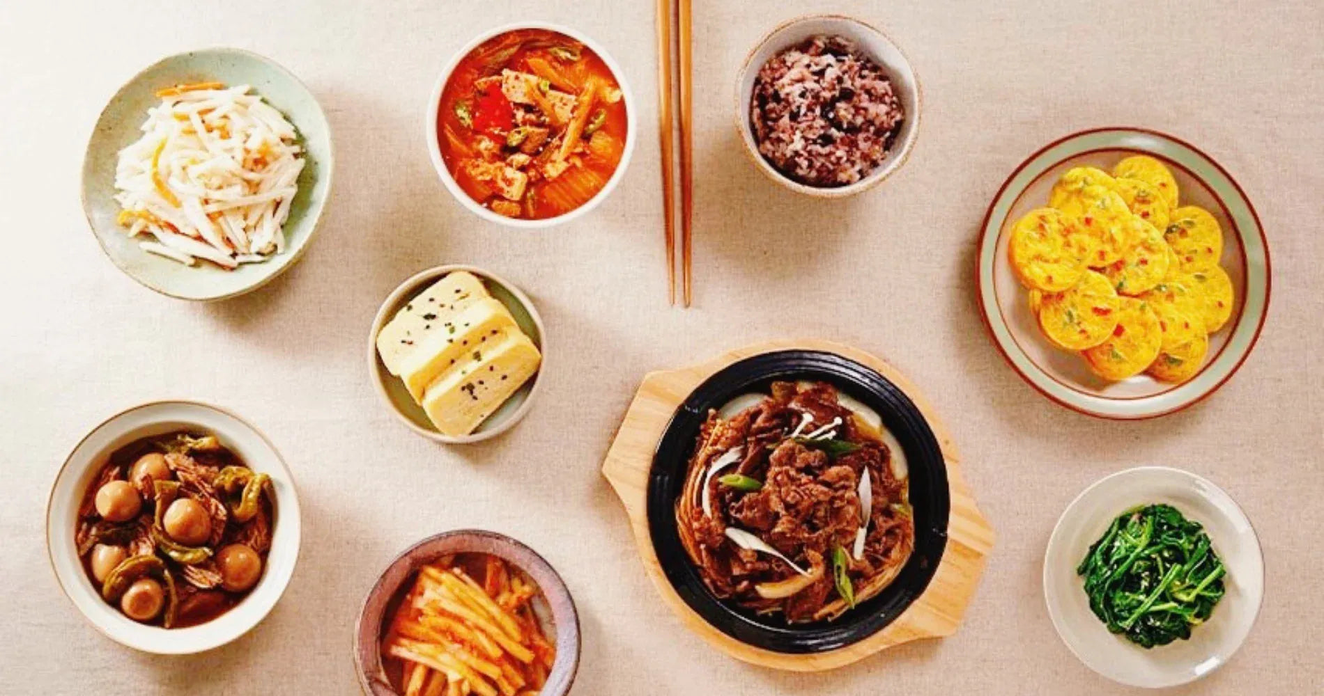 Assorted Korean dishes including beef stew, rice, and various side dishes on a light background