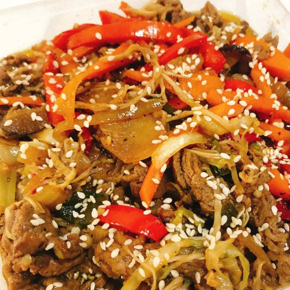 Beef Bulgogi. Stir-fry dish with noodles, vegetables, and sesame seeds on a white plate.