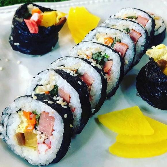 A plate of sliced beef kimbap, which is a type of Korean seaweed rice roll, served with yellow radish.
