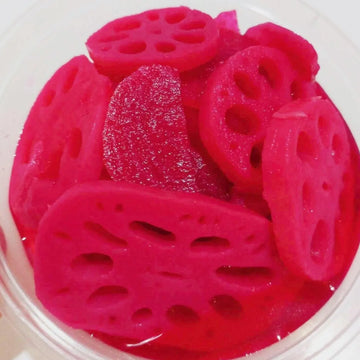 A bowl of pickled lotus root banchan, with a bright red color and a slightly glossy surface.