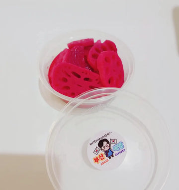Clear container with pickled lotus root banchan on a white background