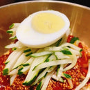 Sliced cucumber and boiled egg on a bed of spicy red sauce in a metal bowl.