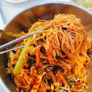Spicy noodles with vegetables in a metal bowl with chopsticks