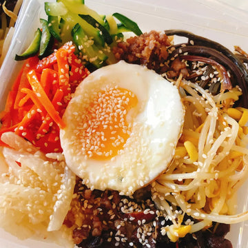 A prepared bibimbap dish with beef, vegetables, and a sunny-side-up egg topped with sesame seeds.