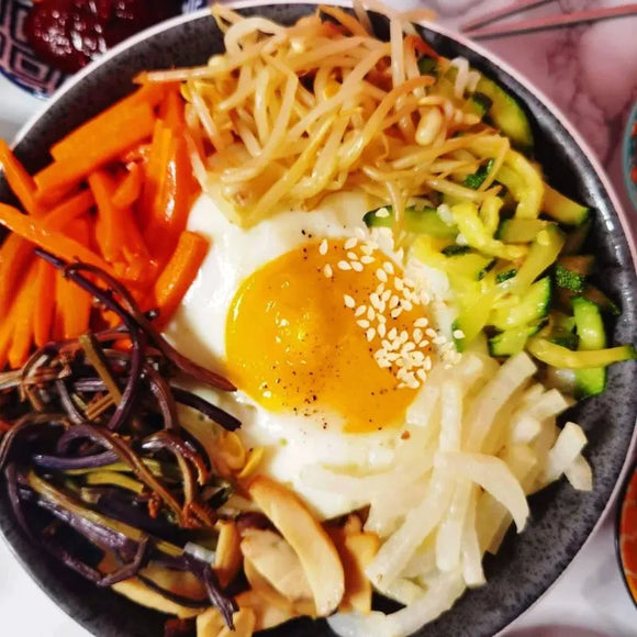 A vegan Korean bibimbap rice bowl topped with steamed seasoned vegetables and a sunny-side-up egg, garnished with sesame seeds.