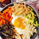 Bowl of bibimbap with various vegetables and a fried egg on a dark plate.