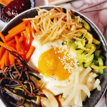 Bowl of bibimbap with various vegetables and a fried egg on a dark plate.