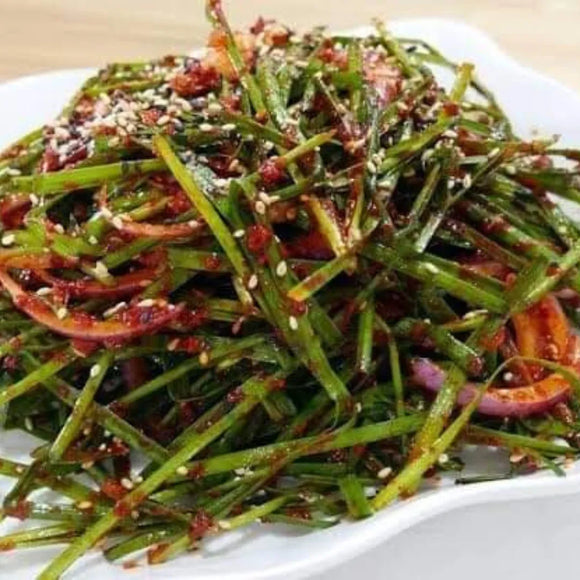 Spicy green herb salad with red chili and sesame seeds on a white plate.
