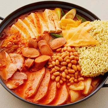 Korean kimchi broth with various ingredients including noodles, vegetables, and sausages in a pot.