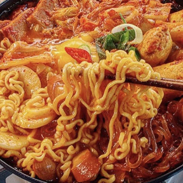 Noodles with vegetables and meat in a Korean kimchi broth, garnished with green onions.