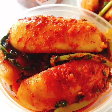 A plate of Chonggak Kimchi, consisting of pickled radishes with long green stems, submerged in a spicy red sauce.