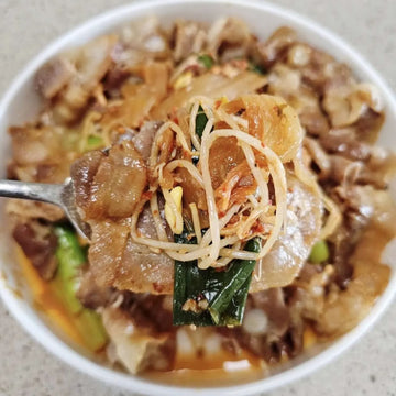 Daepae Samgyup-Bokkeum. Close-up of a bowl of noodles with meat and vegetables, held up by a spoon.
