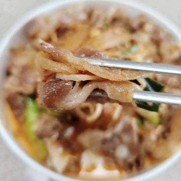 Daepae Samgyup-Bokkeum. Close-up of noodles with meat and vegetables in a bowl, using chopsticks.