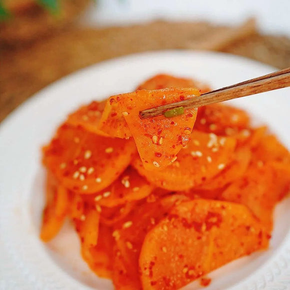 Spicy Seasoned Yellow Pickled Radish slices with sesame seeds on a white plate, held by chopsticks.