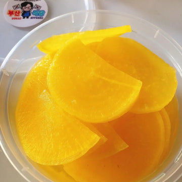 A bowl of yellow pickled radish slices.