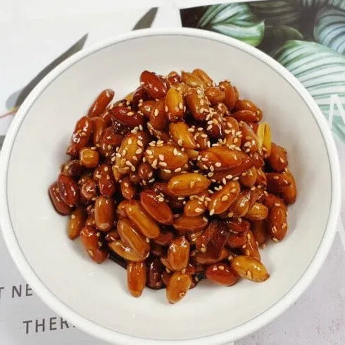 White bowl filled with roasted peanuts and sesame seeds on a white background