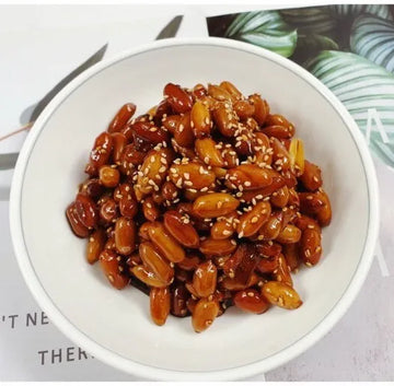 White bowl filled with roasted peanuts and sesame seeds on a light background