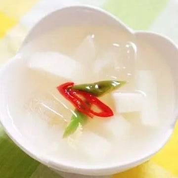 A bowl of dongchimi, which is a type of Korean radish kimchi, garnished with red chili and green scallions.