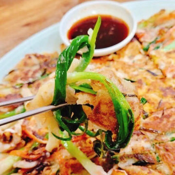 Plated dish of pancake with vegetables and a side of dipping sauce on a wooden table.