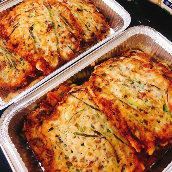 Two foil-tray Korean pancake on a dark surface.