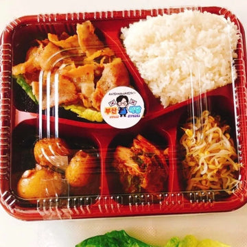 Prepared meal in a red plastic tray with various food items including rice, vegetables, and meat.