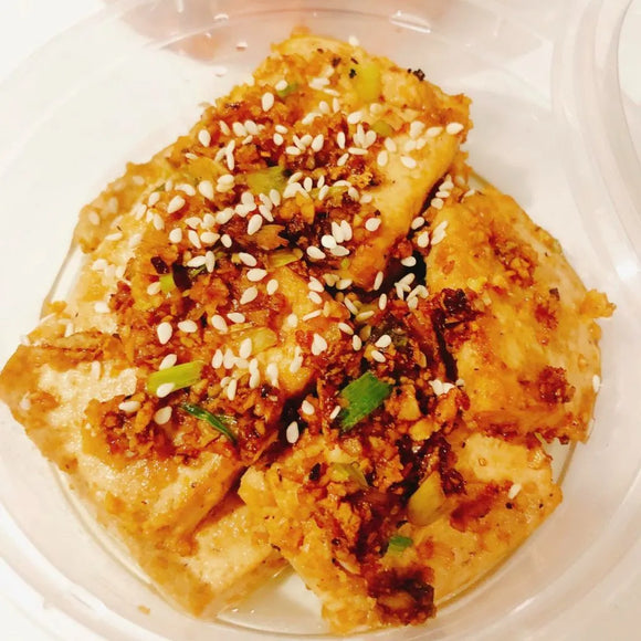 Tofu braised in a savory sauce on a white plate
