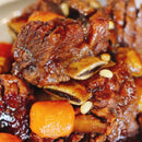 Close-up of braised meat with carrots and pine nuts on a white plate