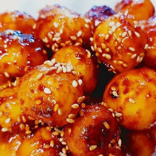 A close-up image of glazed baby potatoes sprinkled with sesame seeds, showing a sticky, savory sauce on the potatoes.