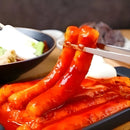garae teokbokki being held with chopsticks over a plate of similar skewers.