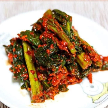 A plate of Gat Kimchi, which consists of fermented mustard greens with a spicy and colorful kimchi sauce.