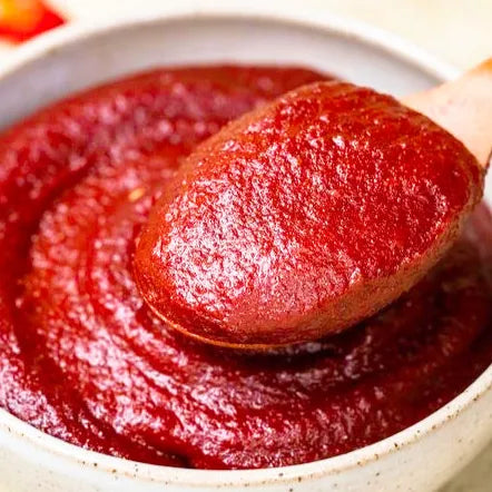 Red chili paste on a wooden spoon over a bowl of red sauce