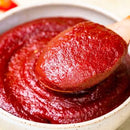 Red chili paste on a wooden spoon over a bowl of red sauce