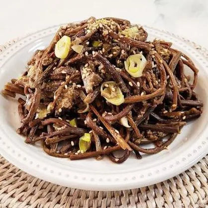 Stir-fried fernbrake with sesame seeds and green onions on a white plate.