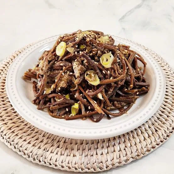 Plated dish of stir-fried fernbrake with vegetables on a woven mat