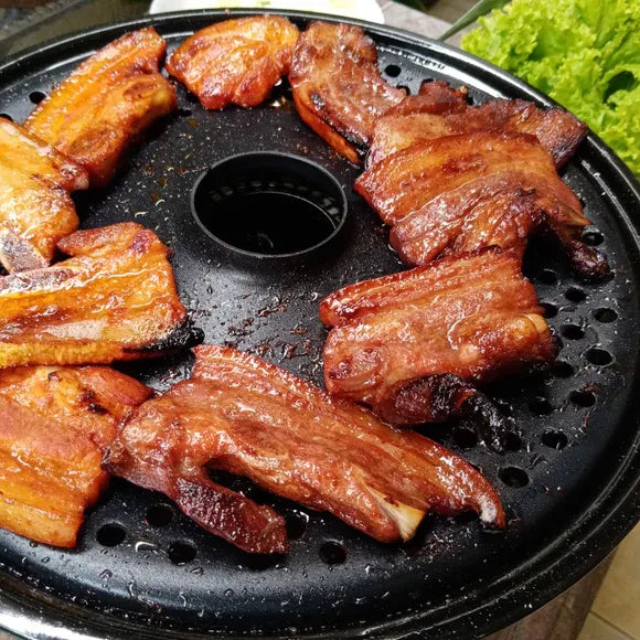 Grilled ribs on a black grill pan with a blurred green leafy vegetable in the background.