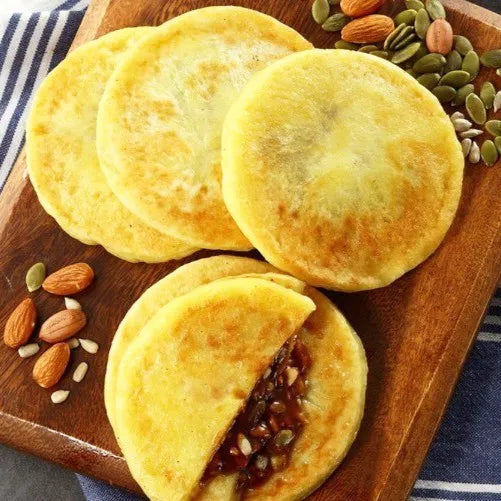 Gyeonghwa Hotteok. Round yellow pastries with a seed filling on a wooden board with nuts and seeds.
