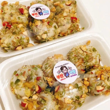 Three containers of traditional tteok loaded with various nuts and seeds with a visible brand sticker on a white background