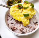White bowl with rice and scrambled eggs topped with green onions on a white plate.
