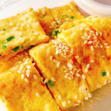A plate of Korean-style soft scrambled eggs garnished with sesame seeds and green onions.