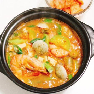 Korean Stew with seafood and vegetables in a black pot on a white background