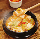 Korean Stew with tofu and vegetables in a black pot on a woven mat.