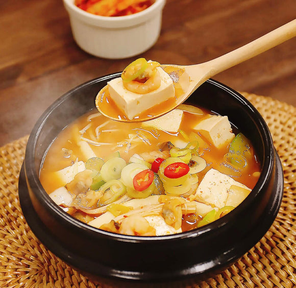 Korean Stew with tofu and vegetables in a black pot on a woven mat.