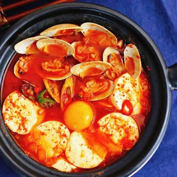 Korean stew simmered in an aromatic, mildly spicy broth with clams and eggs in a red broth on a blue background