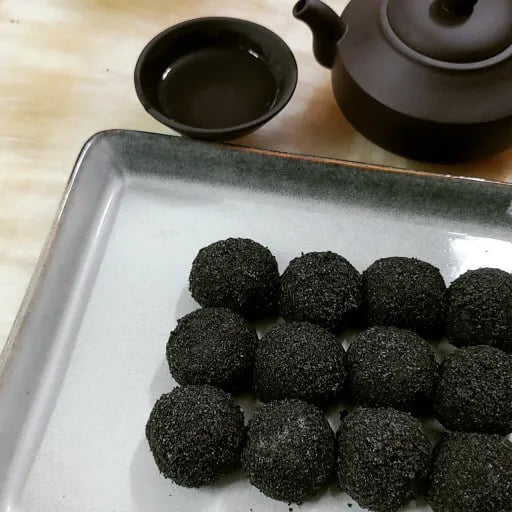 Black sweet rice cake on a white plate with a teapot and cup in the background.