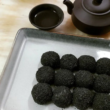 Black sweet rice cake on a white plate with a teapot and cup in the background.