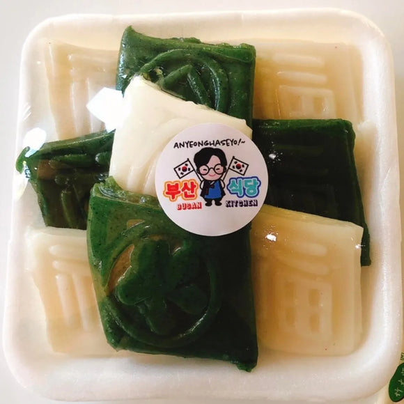 Packaged rice cake with green and white sheets, featuring a label on a white background.