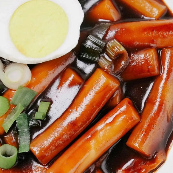 Close-up of tteokbokki on black bean sauce, and a hard-boiled egg.
