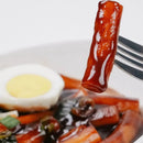 Close-up of a fork with a piece of tteokbokki on black bean sauce